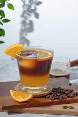 cold Iced black coffee mixed with orange juice and orange slices in glass on wooden plate in white background with nature leaves silhouette shadow. two tones layer fresh summer drink in the morning