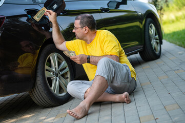 Fototapeta na wymiar worried man sitting on the pavement next to a car near an open fuel tank, fuel price rise concept