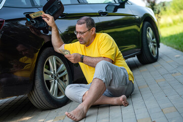 Fototapeta na wymiar worried man sitting on the pavement next to a car near an open fuel tank, fuel price rise concept