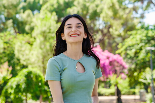 Young brunette woman wearing turquoise tee and orange short on city park, outdoors looking at camera while posing. Natural beauty concept. Beautiful girl. Pretty young woman.