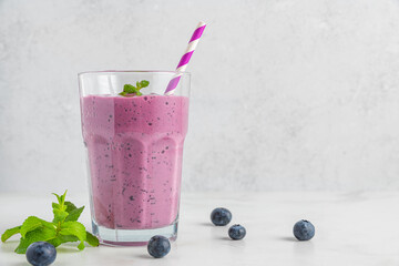 Blueberry smoothie or milkshake in a glass with straw, fresh berries and mint on white background