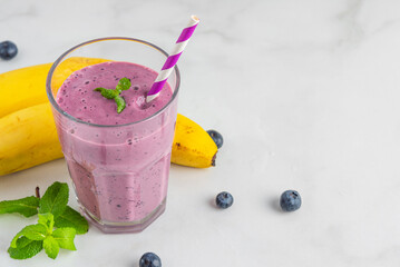 Healthy drink. Blueberry and banana smoothie or milkshake in a glass with straw on white background