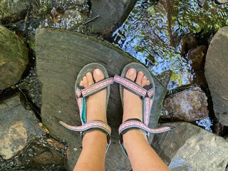 Füße mit Trekkingsandalen auf einem Stein stehen im Bach