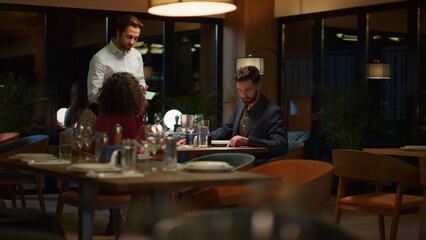 Couple ordering restaurant dinner at night. Waiter serving two lovers on date.