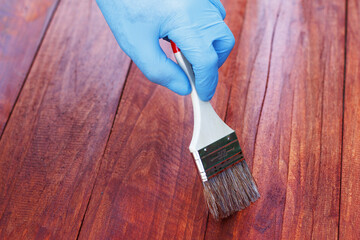 Protective varnishing of a wooden fence in the backyard. Man painting wood stain on wood plank...
