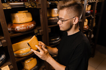 Handsome customer in cheese shop looking at limited gouda cheese. Snack tasty piece of cheese for appetizer.