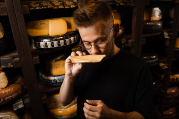 Handsome buyer in cheese shop sniff and enjoy limited gouda cheese. Snack tasty piece of cheese for appetizer.