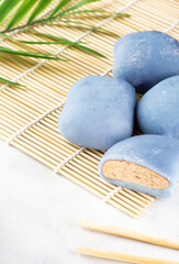 Concept of a traditional Japanese mochi with a maki sudare mat and chopsticks on the table. A Japanese rice cake lying on a wooden mat on white countertop.Asian dessert, mochi ice cream, Asian food