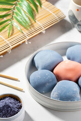 Concept of a traditional Japanese dessert on the kitchen table. A bowl of Japanese mochi with chopsticks and wooden mat on white countertop. Asian rice cake, mochi ice cream, Asian sweet street food.