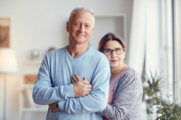 Smiling beautiful senior couple standing in living room and hugging while posing for portrait