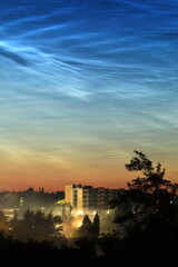 Noctilucent clouds over a city on a foggy night
