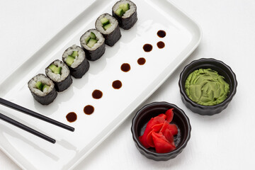Nori sushi with cucumber and black chopsticks on white plate.