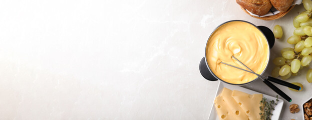 Flat lay composition with pot of delicious cheese fondue on light table, space for text. Banner...