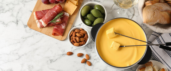 Pot of tasty cheese fondue and snacks on white marble table, flat lay. Banner design