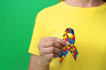 World Autism Awareness Day. Woman with colorful puzzle ribbon on green background, closeup