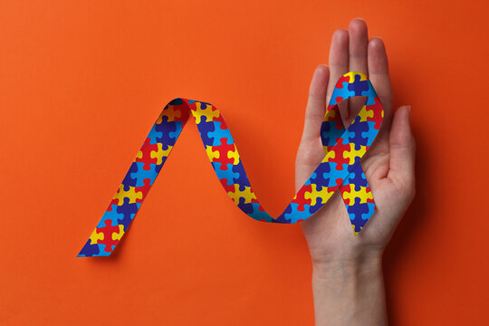 World Autism Awareness Day. Woman with colorful puzzle ribbon on orange background, top view