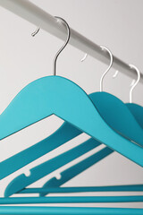 Empty turquoise clothes hangers on metal rail against light grey background, closeup