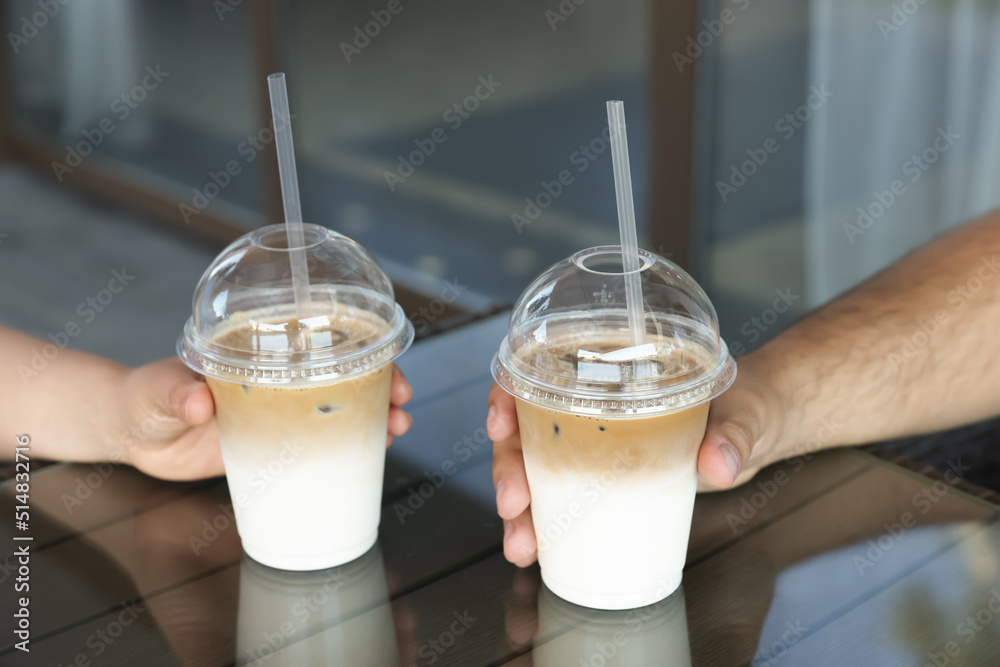 Canvas Prints Man and woman with plastic takeaway cups of delicious iced coffee at table in outdoor cafe, closeup