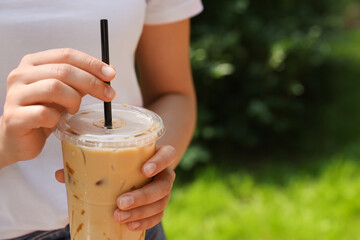 Woman holding takeaway plastic cup with cold coffee drink outdoors, closeup. Space for text