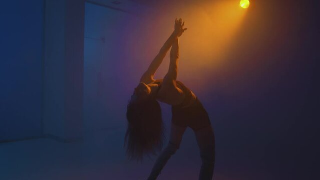 Beautiful graceful girl dancing in colorful studio light in smoke at night. Modern dance, slow motion, handheld video