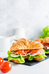 Two croissant sandwiches with ham, cucumbers, tomato and lettuce on a slate. Vertical view