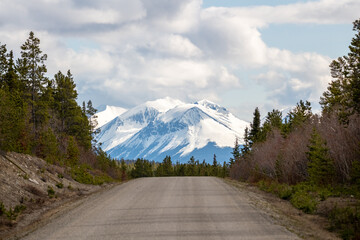 Snow-capped mountains at the end of a dirt road in northern Canada during spring time. Road trip,...