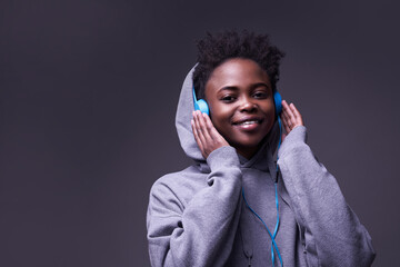 An African-American woman listening to music with headphones.A young woman wearing headphones smiles, looks directly into the camera in a sports uniform on a gray isolated background.High quality phot