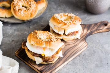 Bagels sandwiches with cheese, fried meat and poached egg on a board. Homemade fast food