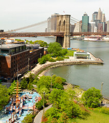 Aerial view of Brooklyn Bridge park with the bridge and Manhattan in the distance - obrazy, fototapety, plakaty