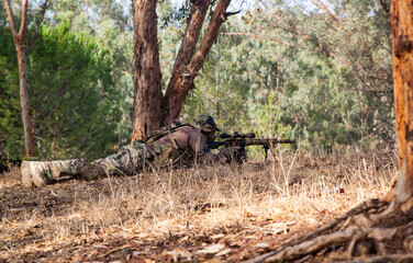 A sniper with a weapon in his hands lies on the ground. A military man aims through the scope of a sniper rifle. A man in camouflage lies on the ground