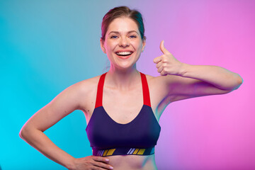 Fototapeta na wymiar Sporty happy young woman in sports bra wear with thumb up. Female fitness portrait isolated on neon color background. Healthy lifestyle concept with yoga instructor.