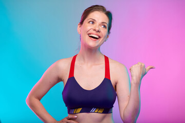 Sporty woman in sports bra pointing away with thumbs up. Female fitness portrait isolated on neon color background. Healthy lifestyle concept with yoga instructor.