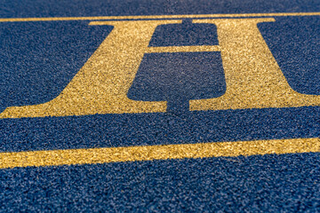 Close up the letter, initial H on a new blue running track with yellow lane lines.