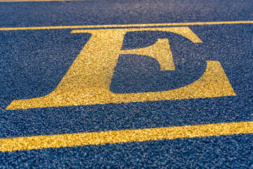 Close up the letter, initial E on a new blue running track with yellow lane lines.