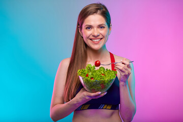 Sporty woman in sportswear green salad in glass bowl and red tomato on fork. Female fitness portrait isolated on neon multicolor background.