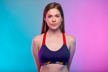 Serious sporty woman in fitness bra sportswear with hands behind back. Female fitness portrait isolated on neon colored background.