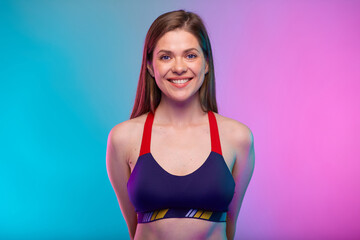 Smiling sporty woman in fitness bra sportswear with hands behind back. Female fitness portrait...