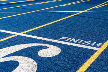 Close up of the finish line on new blue running track with yellow lane lines and other markings.