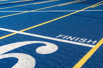 Poster Close up of the finish line on new blue running track with yellow lane lines and other markings. © Thomas