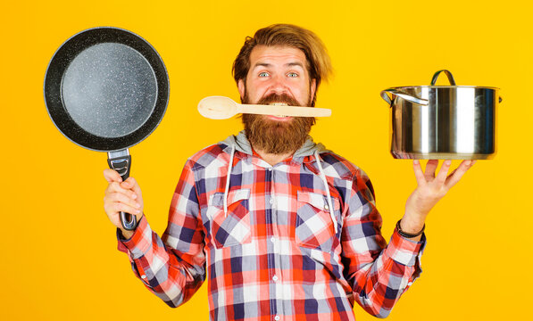 Man With Saucepan And Frying Pan In Hands. Bearded Chef With Wooden Spoon In Mouth. Cooking Utensil.