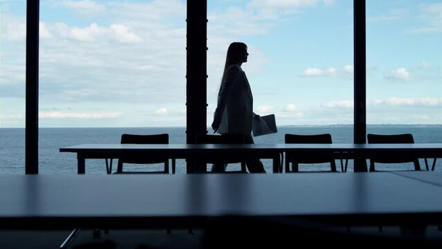 Businesswoman silhouette walking window in office conference room at sea view.
