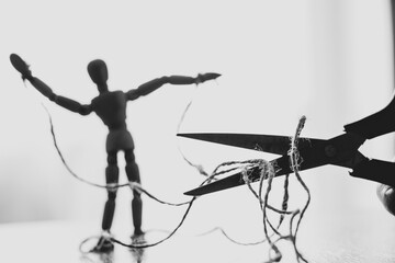 Wooden puppet tied with ropes to the puppeteer and scissors cut the rope, manipulation of people...