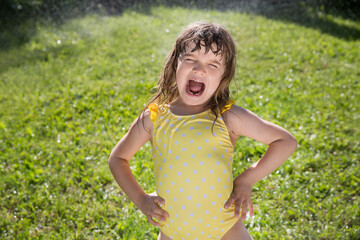 Happy child girl playing with garden hose and having fun with spray of water in sunny backyard....