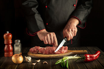 Chef cuts raw veal meat on a cutting board before baking. Cooking delicious food in the kitchen - obrazy, fototapety, plakaty