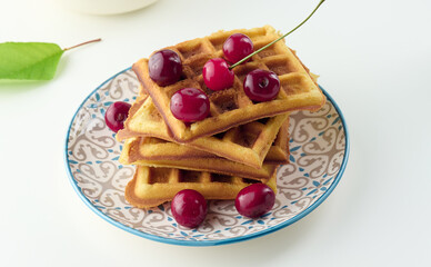 Stack of baked Belgian waffles with ripe red cherries on the white table, breakfast.