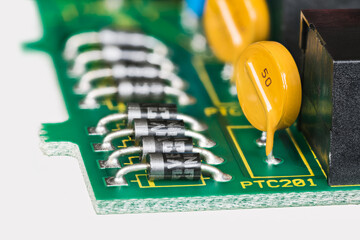 Semiconductor diodes and yellow resettable fuses in PCB detail on white background. Closeup of electronic components as diode or round polymeric PTC device - polyswitch on green printed circuit board. - obrazy, fototapety, plakaty