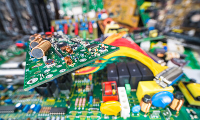 Obraz premium Circuit board on blur e-waste pile of discarded electric and computer devices. Air or ferrite core coils, chips or small components on cable TV amp PCB detail. Waste recycling in electronics industry.