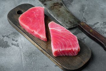 Obraz na płótnie Canvas Fresh raw tuna steak, on wooden cutting board, and old butcher cleaver knife, on gray stone background , with copyspace and space for text