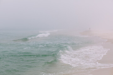 A man walks along the beach in Pensacola, FL alone and isolated in the fog and mist. 