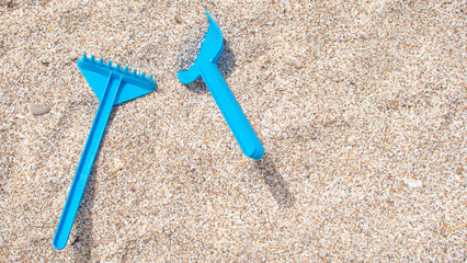 Fototapeta na wymiar Blue toy plastic shovel and rake on the white sand of the beach